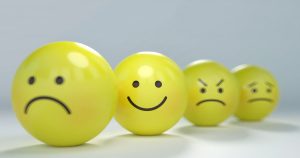Four yellow, egg-shaped figures with drawn-on faces, from left to right: sad with a frown, happy with a smile, angry with furrowed brows, and worried with a slight frown.